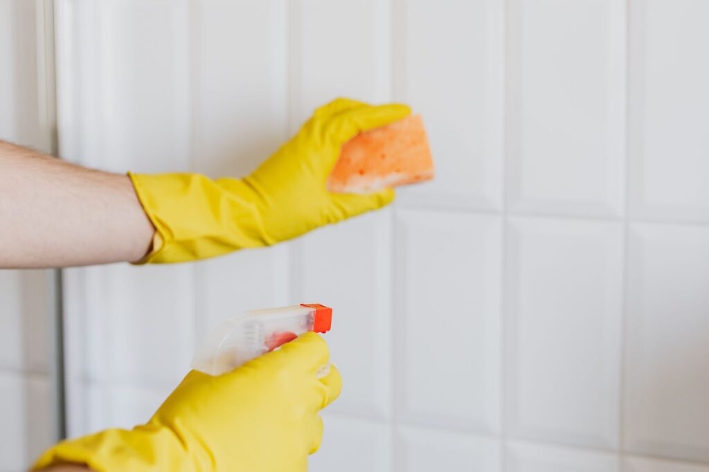 Limpieza de azulejos blancos con esponja, spray y guantes de goma