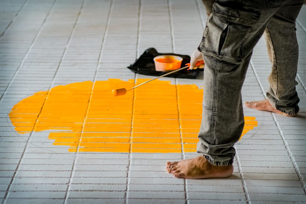 Persona pintando baldosas del suelo con un rodillo de mango largo
